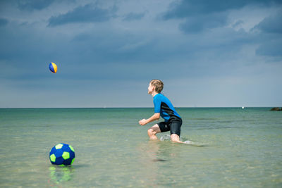 Boy playing with ball in sea against sky