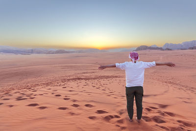 Rear view of man standing at beach against clear sky during sunset