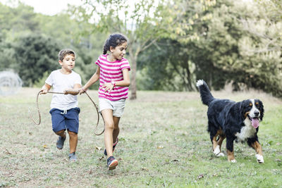 Two kids running and playing with a mountain dog