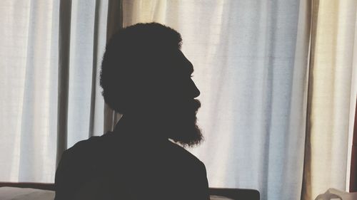 Silhouette man against curtains hanging on window at home