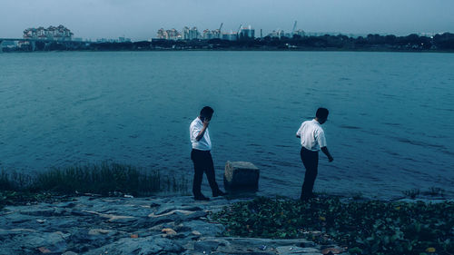 Rear view of people standing at sea shore against sky