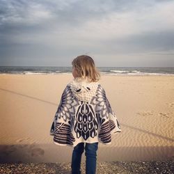 Rear view of girl wearing scarf at beach against cloudy sky