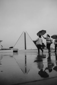 People on wet road against sky during rainy season