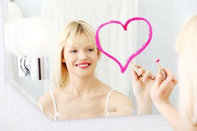 Young woman making heart shape on mirror in bathroom