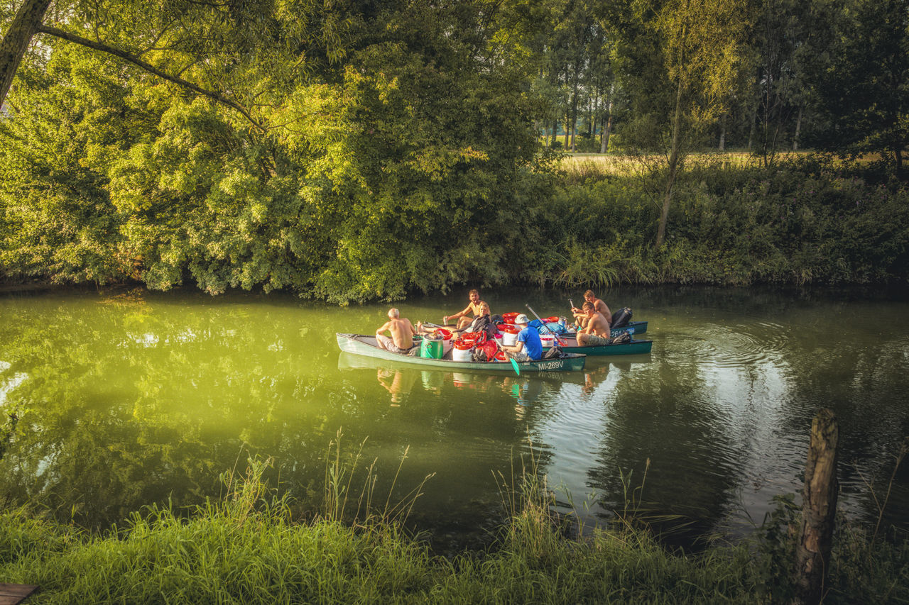 PEOPLE SITTING IN LAKE AGAINST TREES