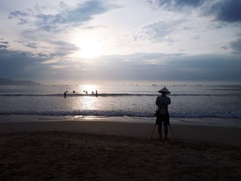 Rear view of silhouette man standing on beach during sunset