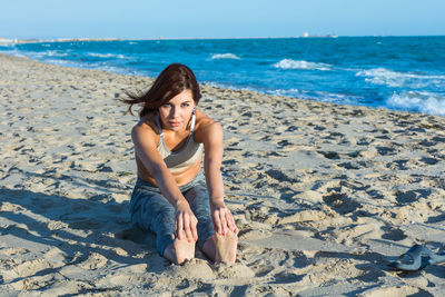 Young woman sitting on shore at beach against sky