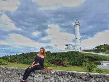 Portrait of smiling young woman by lighthouse against sky