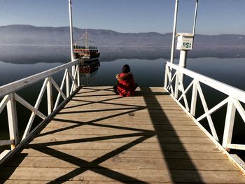 Rear view of woman sitting on railing against sea