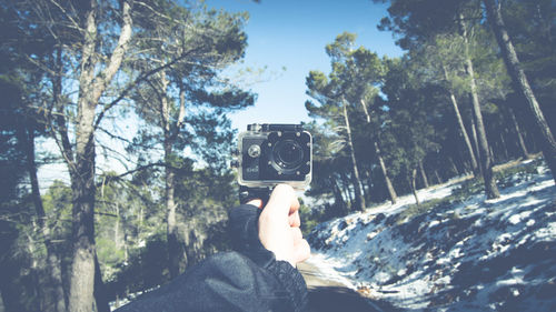 Low section of woman photographing by trees against sky