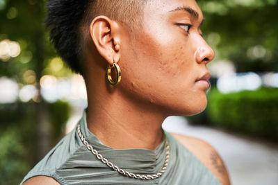 Calm filipino non binary person with pimples on face looking away on blurred background of park in summer