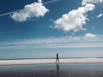 Rear view of man walking on beach against sky