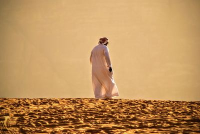 Rear view of man in traditional clothing walking on sand