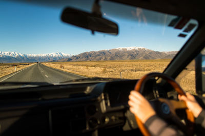 Cropped hand of woman driving car by against sky