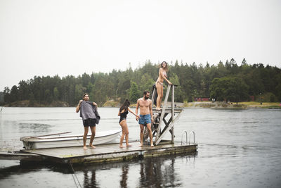 Male and female friends standing on jetty over lake against clear sky during weekend getaway