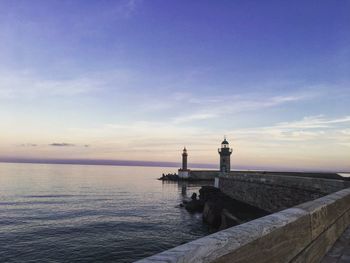 Lighthouse by sea against sky during sunset