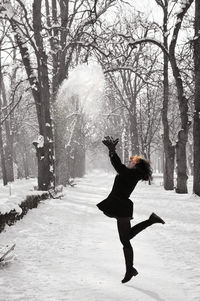 Full length of woman playing with snow in forest