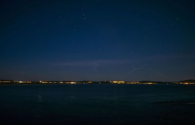 Illuminated city by sea against sky at night