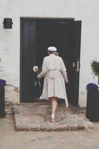 Rear view of woman holding flowers while entering house