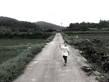 Full length of boy walking on walkway while holding toy amidst field