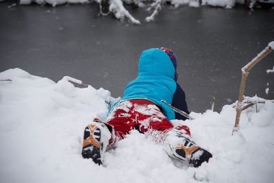 Child in warm clothing lying at snow covered lakeshore