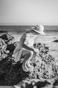 Woman sitting on rock at sea against sky
