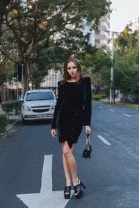 Portrait of young woman standing on road in city