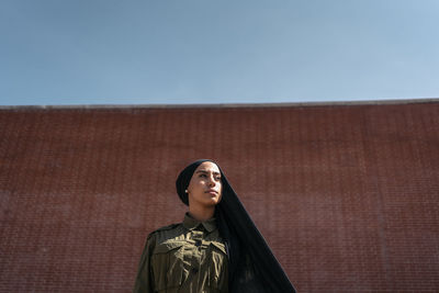 Portrait of young woman standing against blue sky