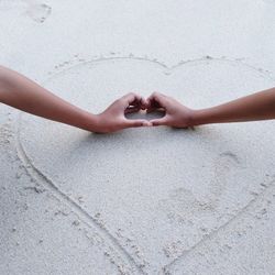 High angle view of hand holding hands on sand between two friend