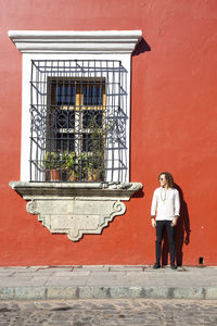 Man standing next to a big window of a red colonial building in mexico