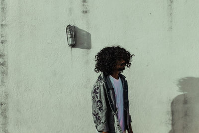 Woman looking away while standing against wall