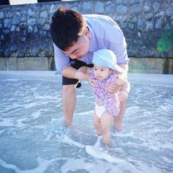 Smiling young man holding his daughter in water on shore at beach