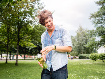 Laughing man douses himself with water from bottle. staying cool in summer. wet fun in urban park. 