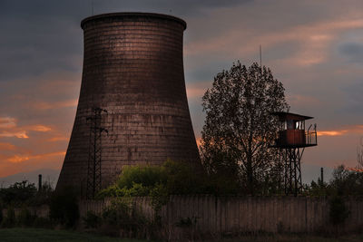 Low angle view of factory against sky at sunset