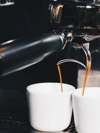 Close-up of machinery pouring coffee in cups at cafe