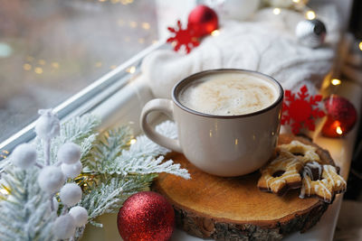 Hot coffee cup on a frosty winter day window background with cookies, christmas holiday