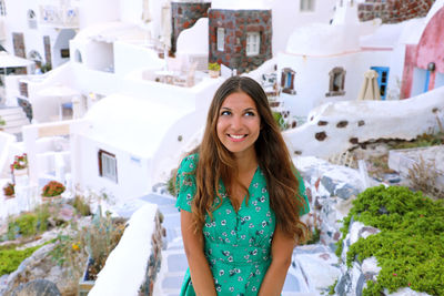 Portrait of smiling young woman standing against buildings