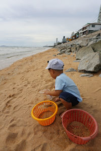 Full length of boy on wicker basket on beach