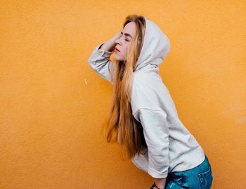 Young woman in hood standing against yellow wall