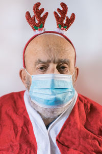 Elderly man in santa claus suit wearing a face mask and reindeer ears