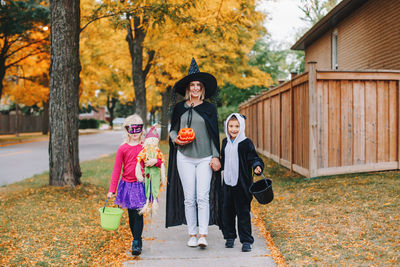 Full length portrait of mother with kids standing on tree during autumn