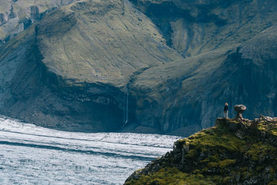 Man standing on cliff by sea against sky