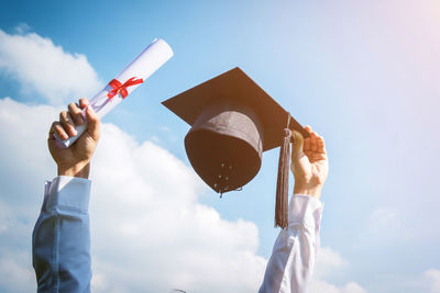 Low angle view of person hand holding certificate with mortarboard