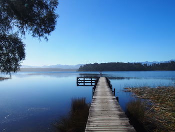 Pier over lake against clear blue sky