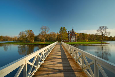 Empty footbridge over lake against clear blue sky during sunset