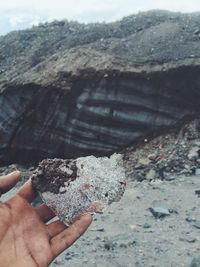 Close-up of hand holding sand on rock at beach