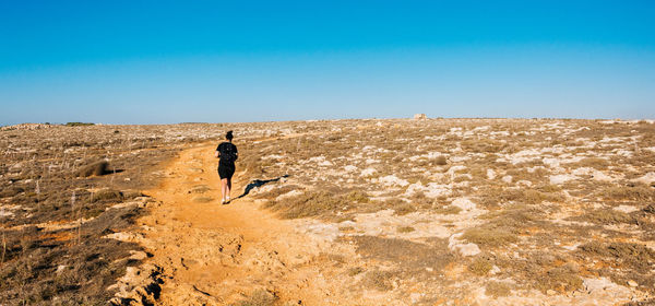 Rear view of woman walking on pathway against clear blue sky