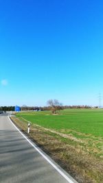 Road amidst field against clear blue sky