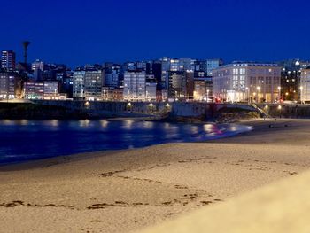 Illuminated buildings by sea against clear sky at night