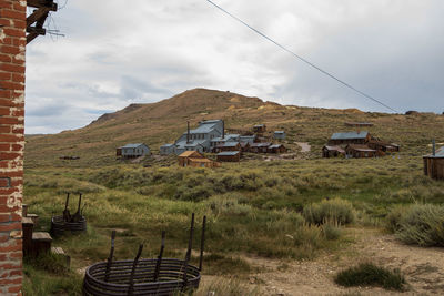 Houses and buildings of ghost town on hillside on field against sky